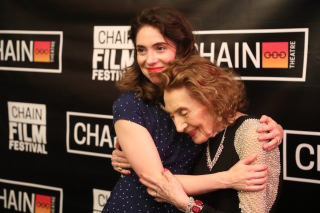 Two woman embrace in front of a step-and-repeat. 